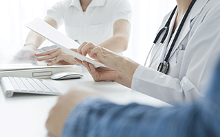 Medical Administrative Assistant handing paperwork to a doctor