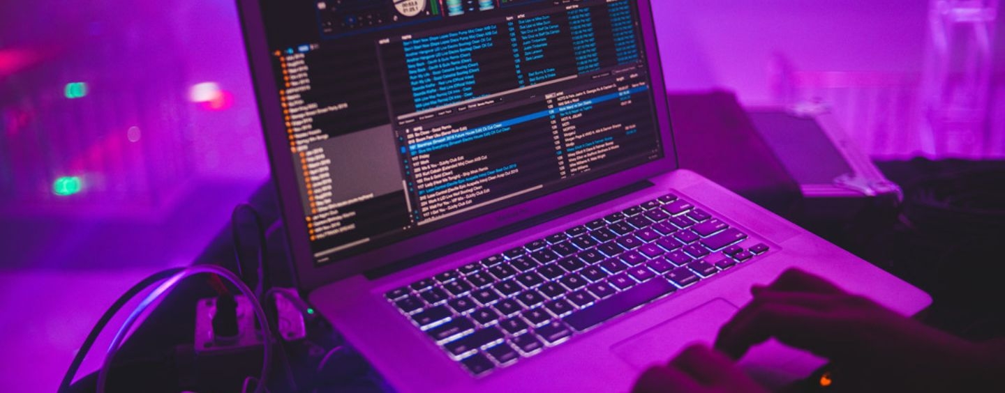 Laptop connected with code on screen connected to sound system, bathed in purple light