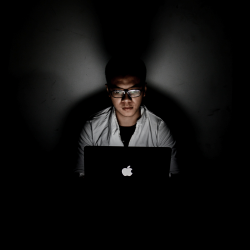 Hacker working in the dark with his face lit by a laptop screen.