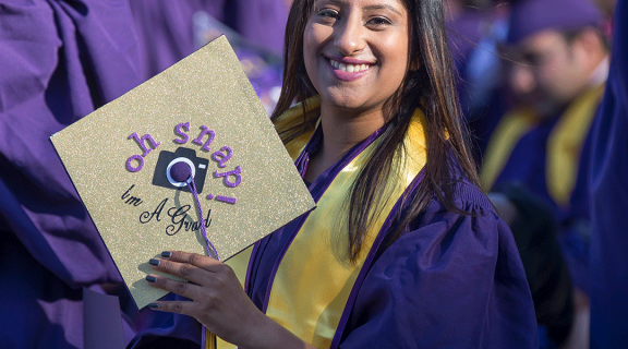 Graduate at Commencement. Her cap says "Oh, snap! I'm a grad." with a camera.