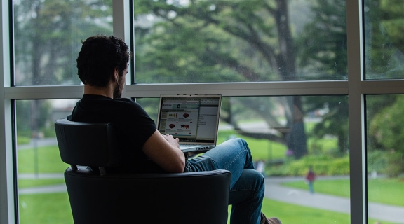 Student taking online class in the library, with a view of campus